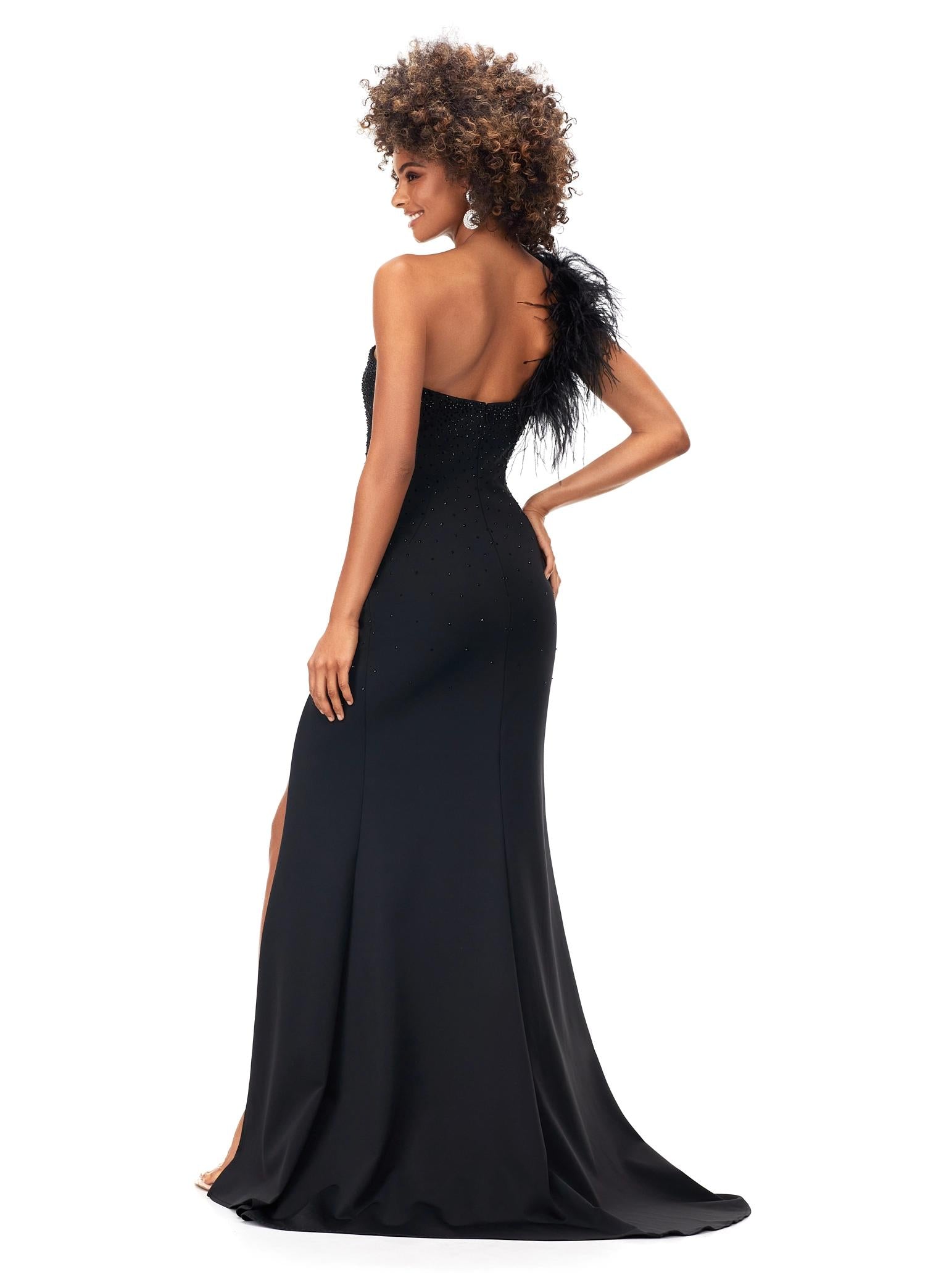 Back. Black ASHLEYlauren 1129 one shoulder scuba gown featuring feather-embellished neckline, heat set stones cascading down the skirt, and a left leg slit for a bold and elegant look.