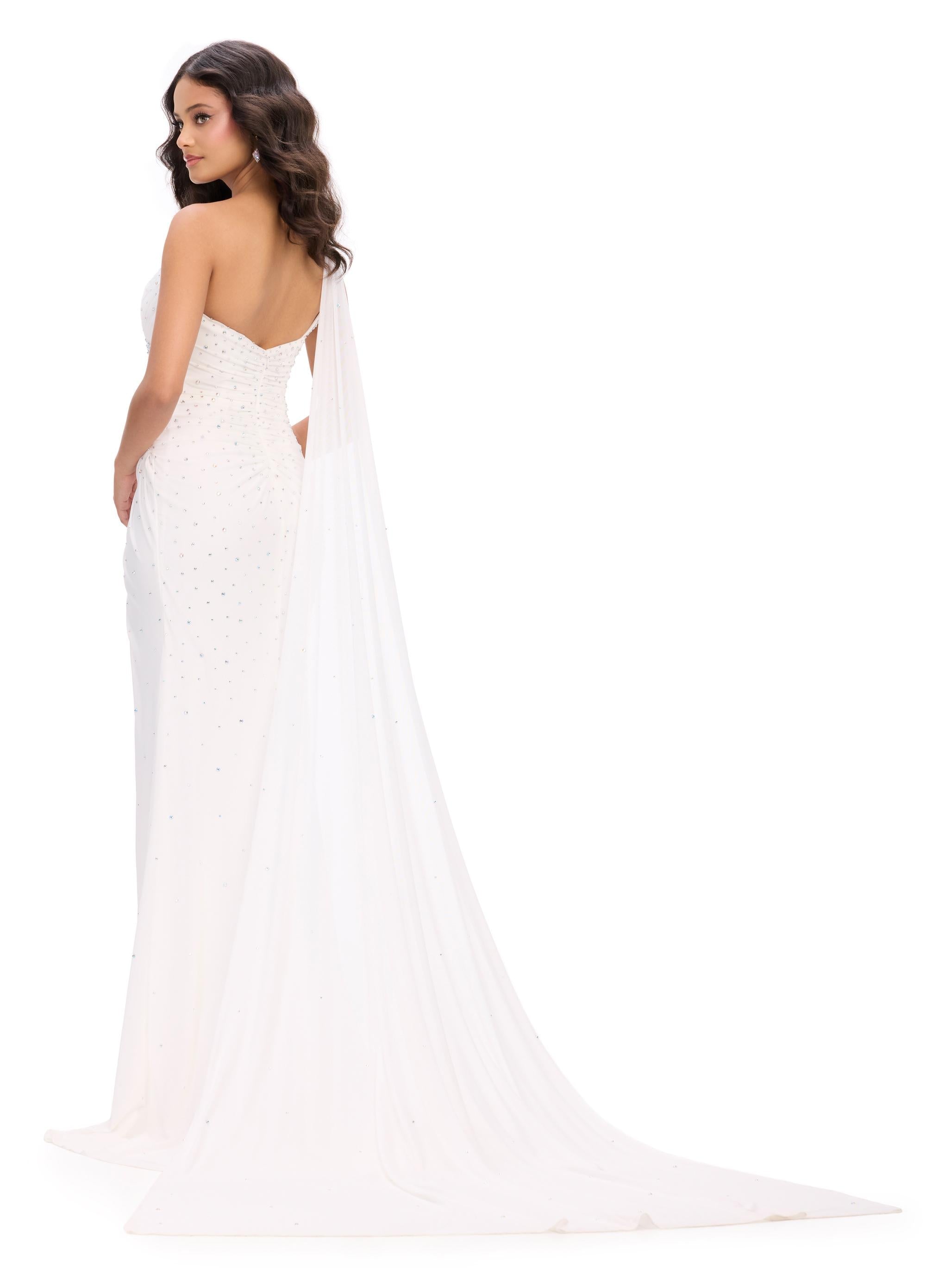 Back. White ASHLEYlauren 11736 glamorous one shoulder gown featuring press-on stone embellishments, a dramatic one shoulder cape, and a left leg slit for an elegant and show-stopping look.