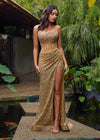 Editorial. Gold ASHLEYlauren 11236 jaw-dropping strapless gown featuring a fitted silhouette, corset bustier with stunning crystal beadwork, a fully beaded wrap skirt, and a left leg slit for a glamorous red carpet-worthy look.